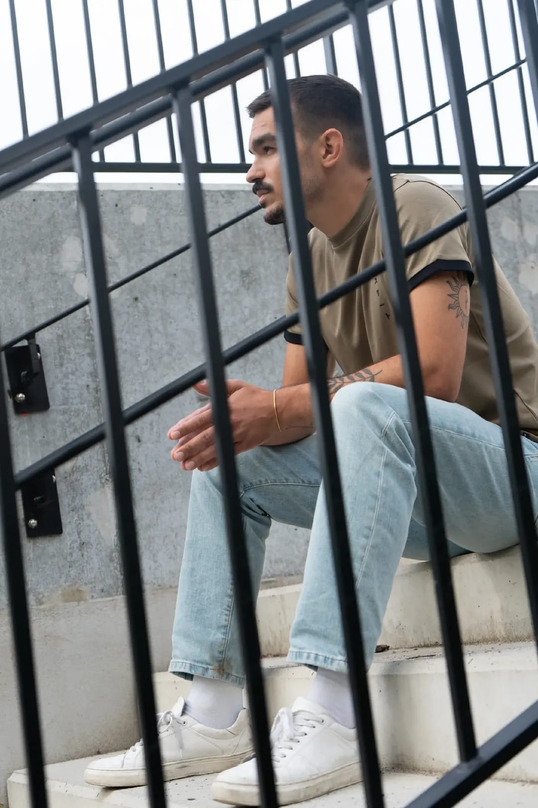 Man in an olive Asurito ringer tee on concrete stairs